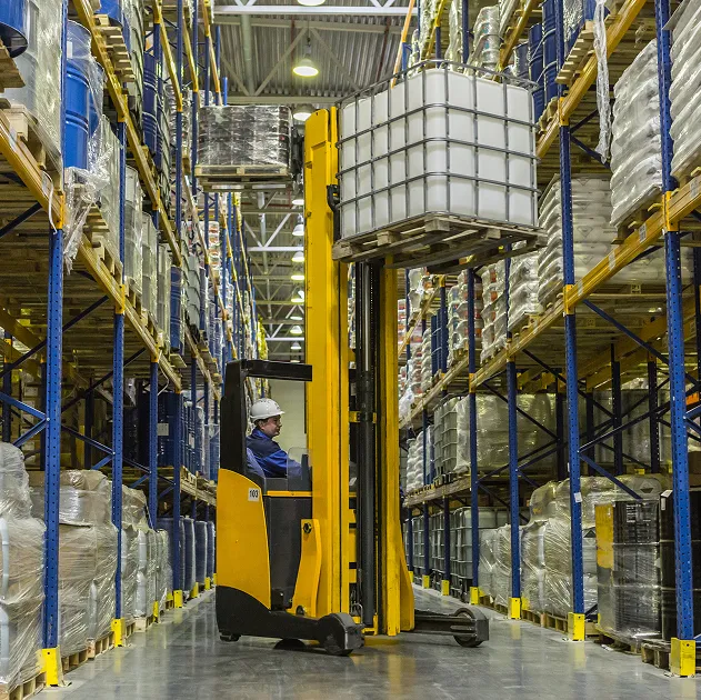 Montacargas elevando un contenedor IBC blanco en los pasillos de un almacén logístico de productos químicos industriales.